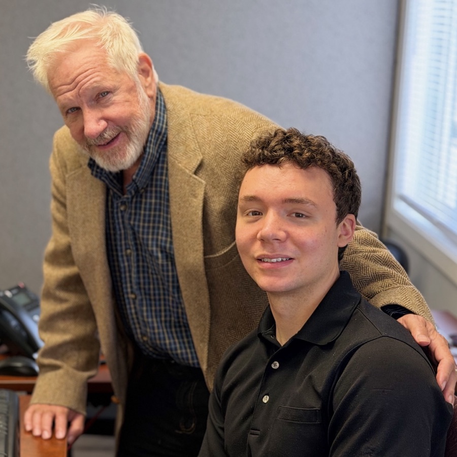 Mike Deziel seated at a desk with Mark Deziel standing at his shoulder